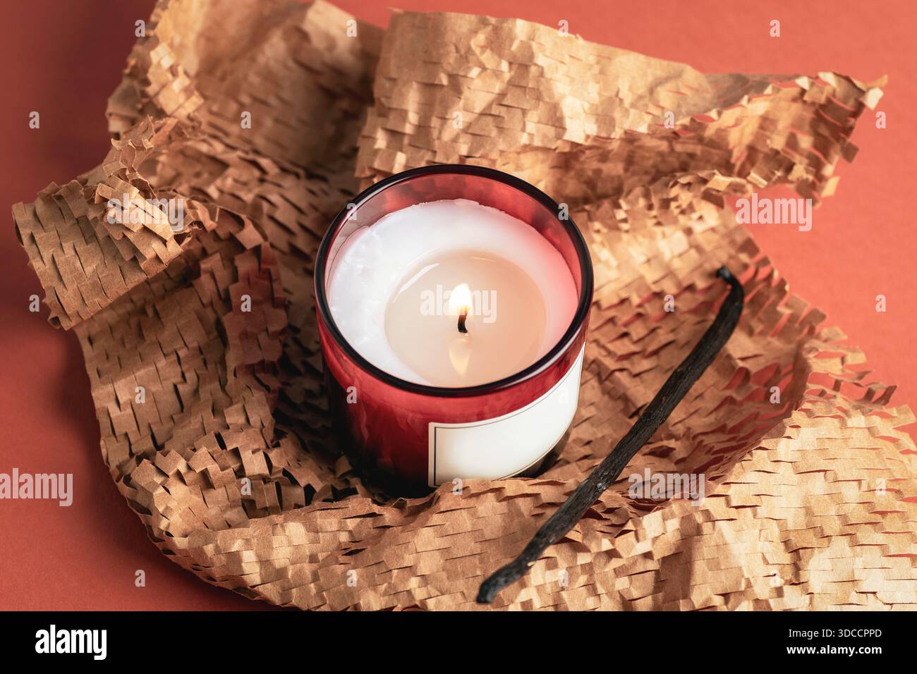 Bougie parfumée allumée dans un pot en verre avec gousse de vanille enveloppée dans du papier kraft texturé sur fond orange chaud. Vue de dessus. Banque D'Images