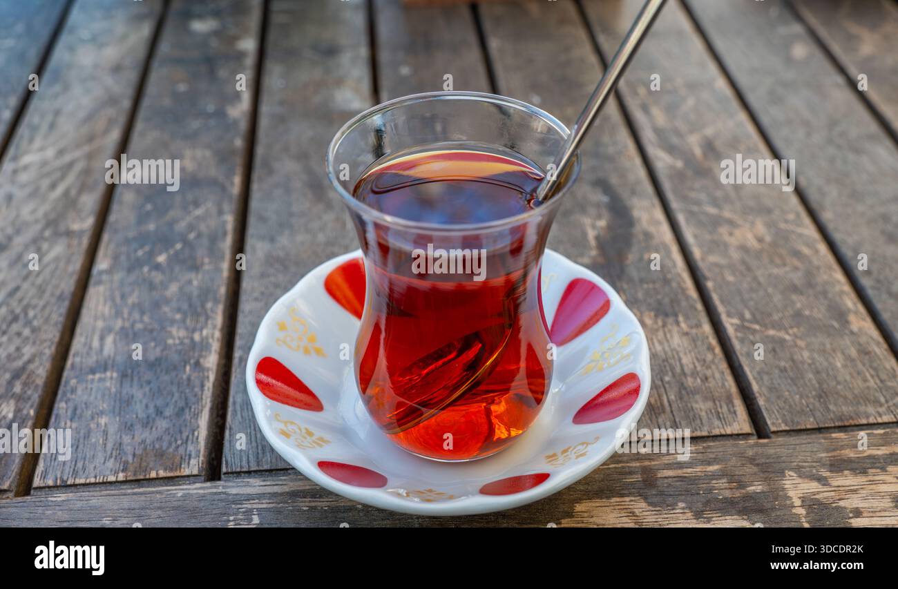 Gros plan du thé turc traditionnel (Cay) servi dans un verre en forme de tulipe avec une cuillère sur une table en bois. Banque D'Images