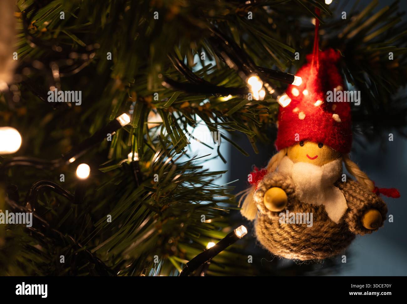 Gros plan d'un ornement de gnome de Noël fait à la main accroché à un arbre décoré avec des lumières de fée chaudes, créant une atmosphère de vacances confortable et festive. Banque D'Images