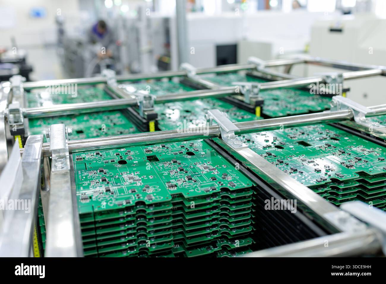 Cartes de circuits imprimés vertes dans des racks métalliques sur un convoyeur à l'intérieur d'une usine électronique montrant l'assemblage automatisé de gros volumes et le contrôle de processus Banque D'Images