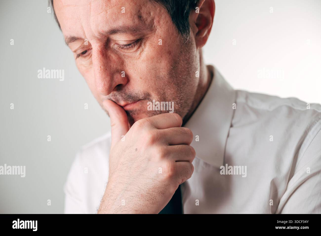 Portrait d'un homme d'affaires d'âge moyen, regardant vers le bas avec la main pensivement sur le menton, profonde inquiétude gravée sur son visage, pour crise financière, bavure mentale Banque D'Images