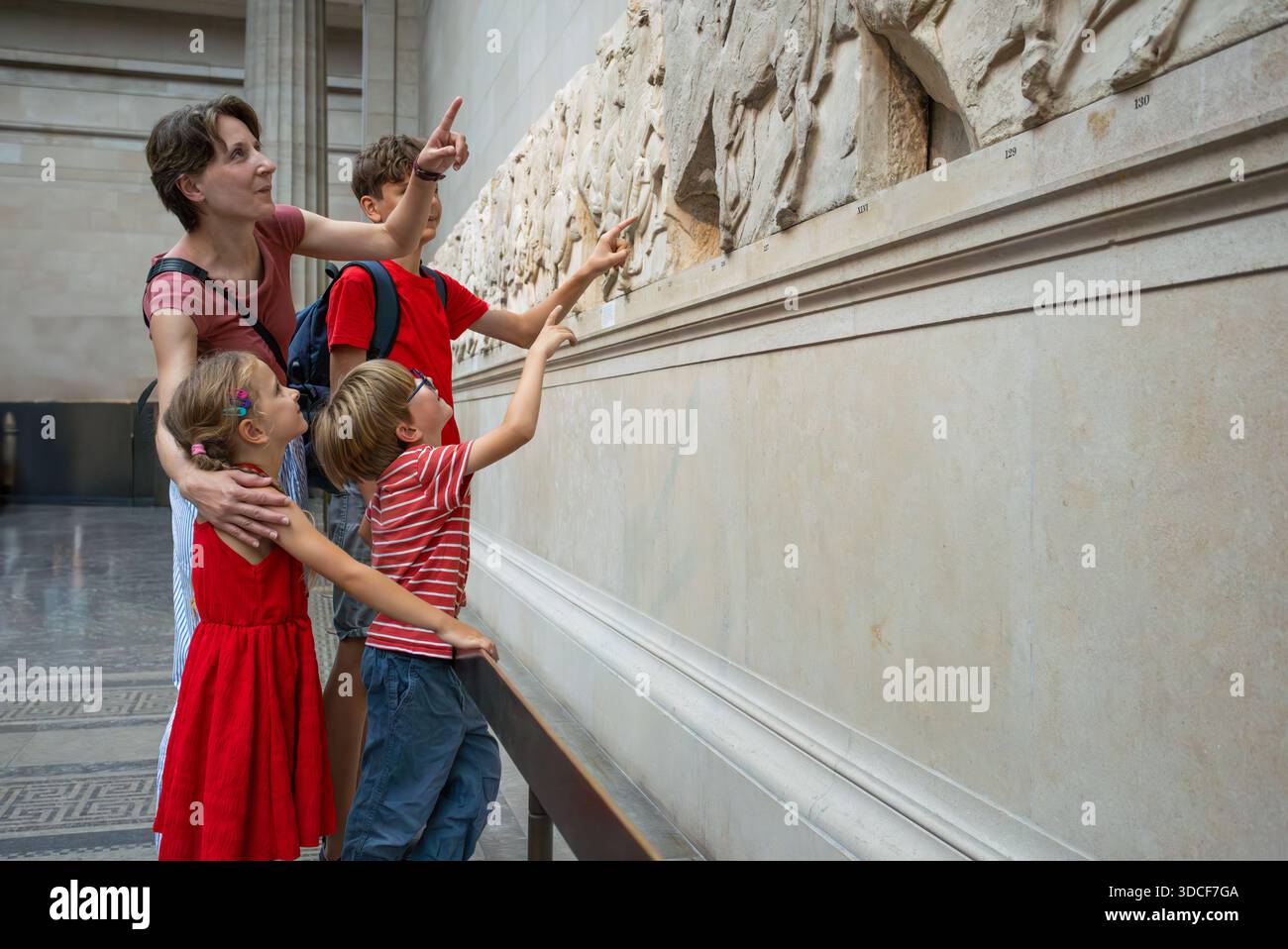 Dans une galerie, une femme et ses enfants examinent une sculpture ancienne, faisant des gestes vers les détails complexes Banque D'Images