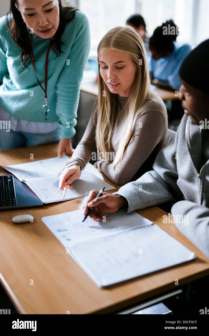 Vue sous un angle élevé de la résolution de l'équation mathématique avec l'aide d'une enseignante dans une salle de classe universitaire Banque D'Images