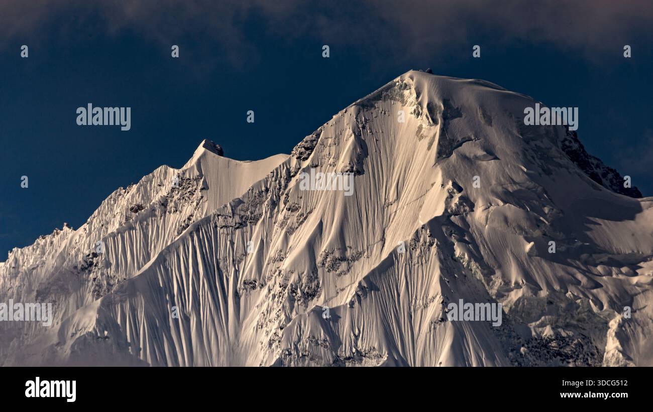 Vue sur les sommets enneigés transperçant le ciel clair et net, leurs crêtes dentelées et leurs ombres profondes contrastant avec la neige lisse et ensoleillée de Hunza Banque D'Images