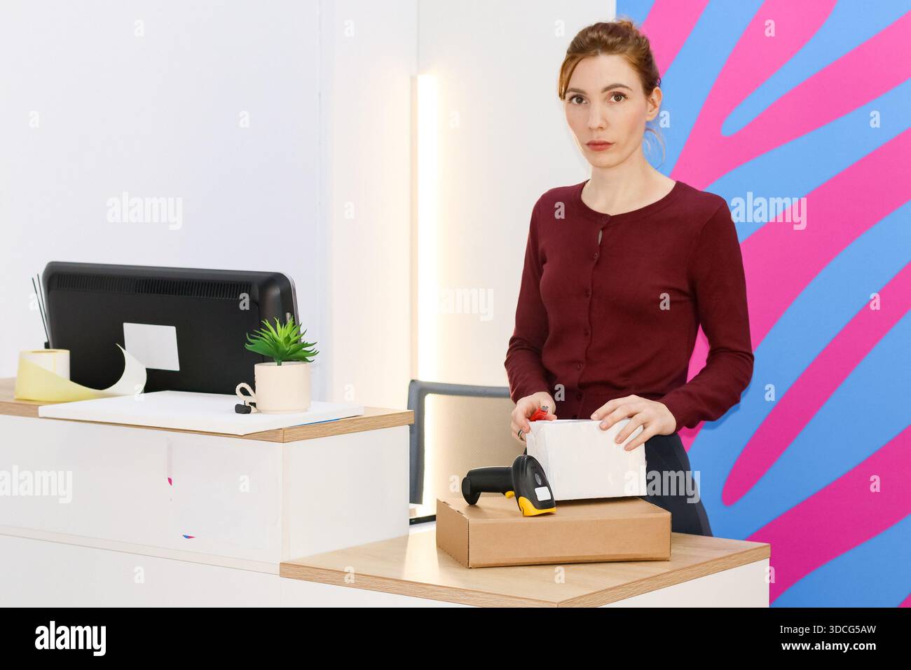 Employé en chandail Bordeaux tenant le colis et le lecteur de code-barres sur carton dans la zone de ramassage. Banque D'Images