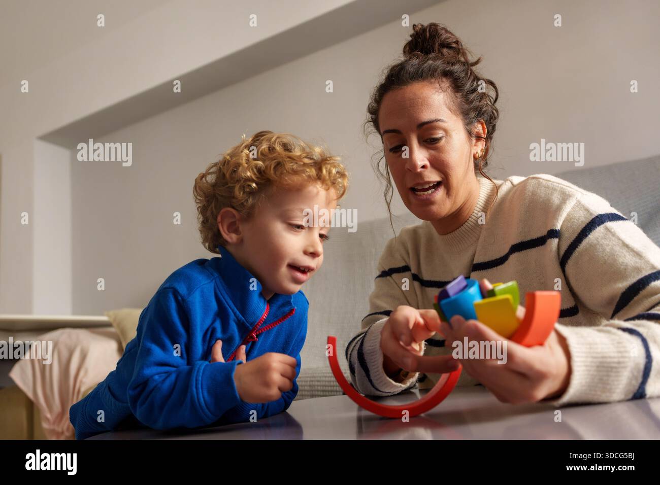 Heureuse mère et garçon en bas âge s'engageant avec un jouet d'équilibrage en bois coloré, profitant du temps de qualité en famille et du développement de la petite enfance Banque D'Images