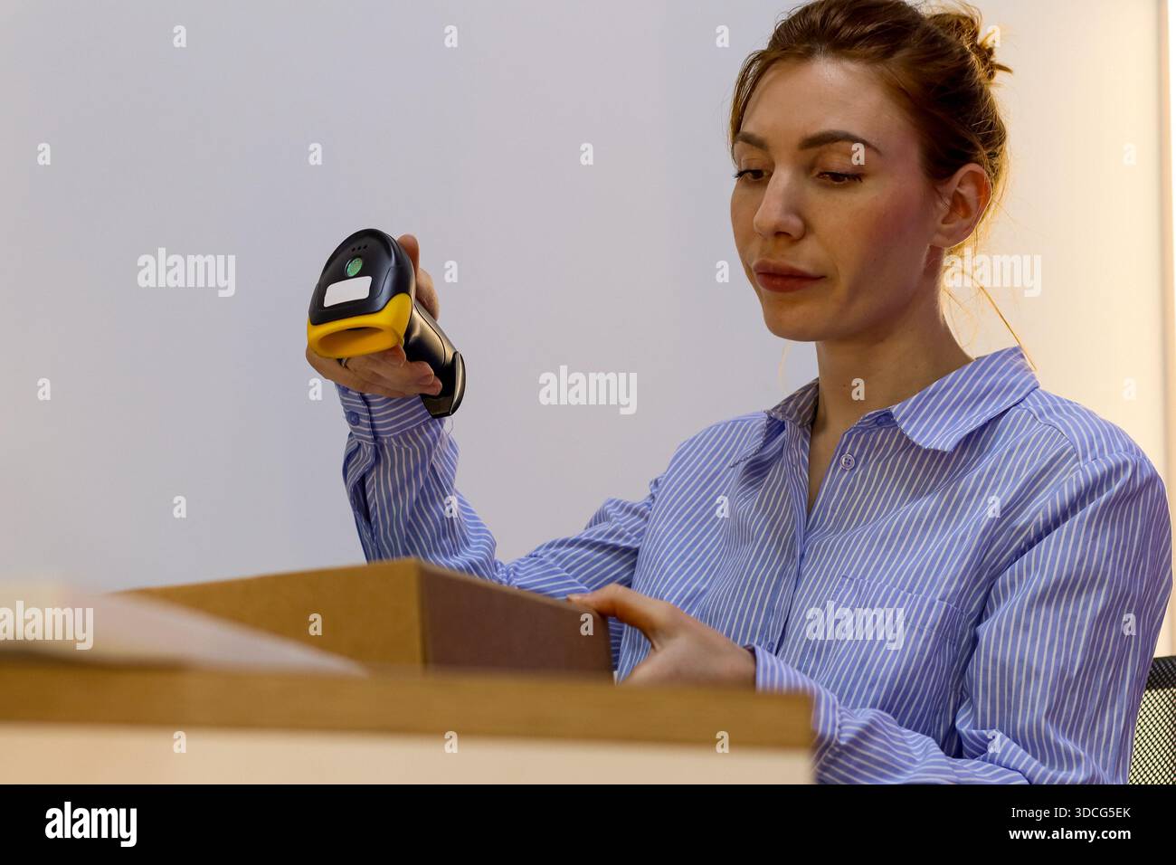 Le membre du personnel soulève le lecteur de codes-barres portatif tout en manipulant le paquet de carton au poste de correspondance. Banque D'Images