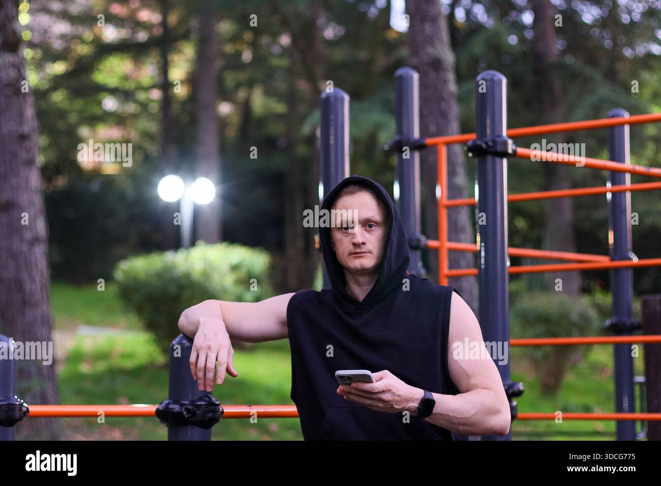 Vue avant de l'homme en forme s'appuyant sur le bar vérifiant le téléphone dans le terrain de jeu du parc Banque D'Images