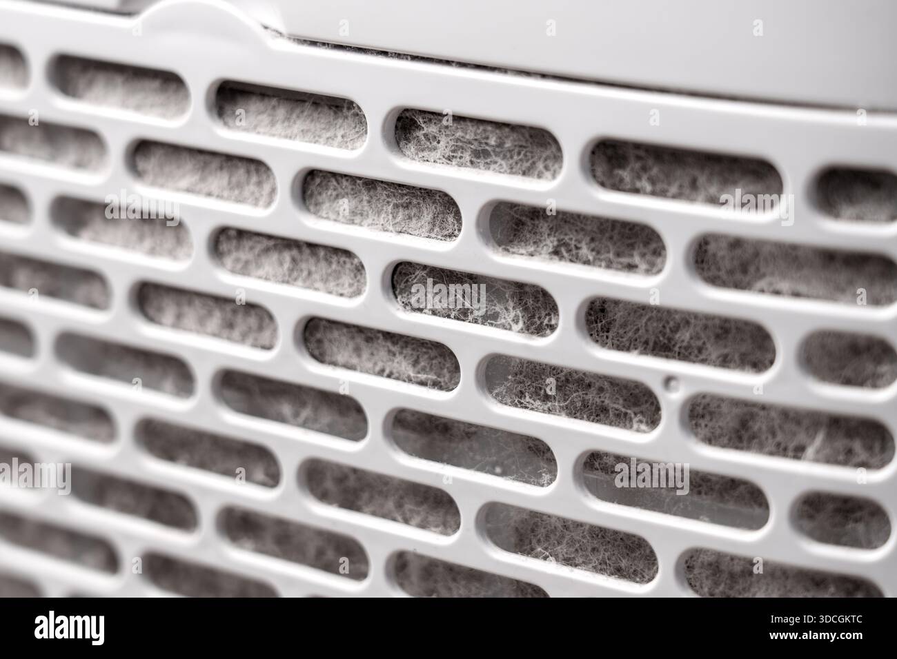 Filtre d'admission obstrué dans le purificateur d'air domestique avec des couches épaisses de poussière accumulée et de fibres sur une grille de ventilation en plastique Banque D'Images
