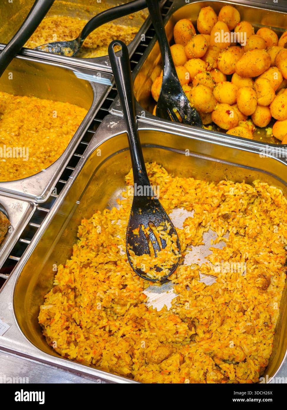 Buffet libre-service avec plateaux en acier inoxydable remplis de riz épicé, sauce au curry et pommes de terre assaisonnées, prêt à servir dans une cantine Banque D'Images