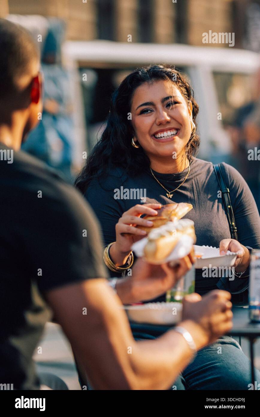 Heureuse jeune femme mangeant de la restauration rapide avec un ami dans la rue Banque D'Images
