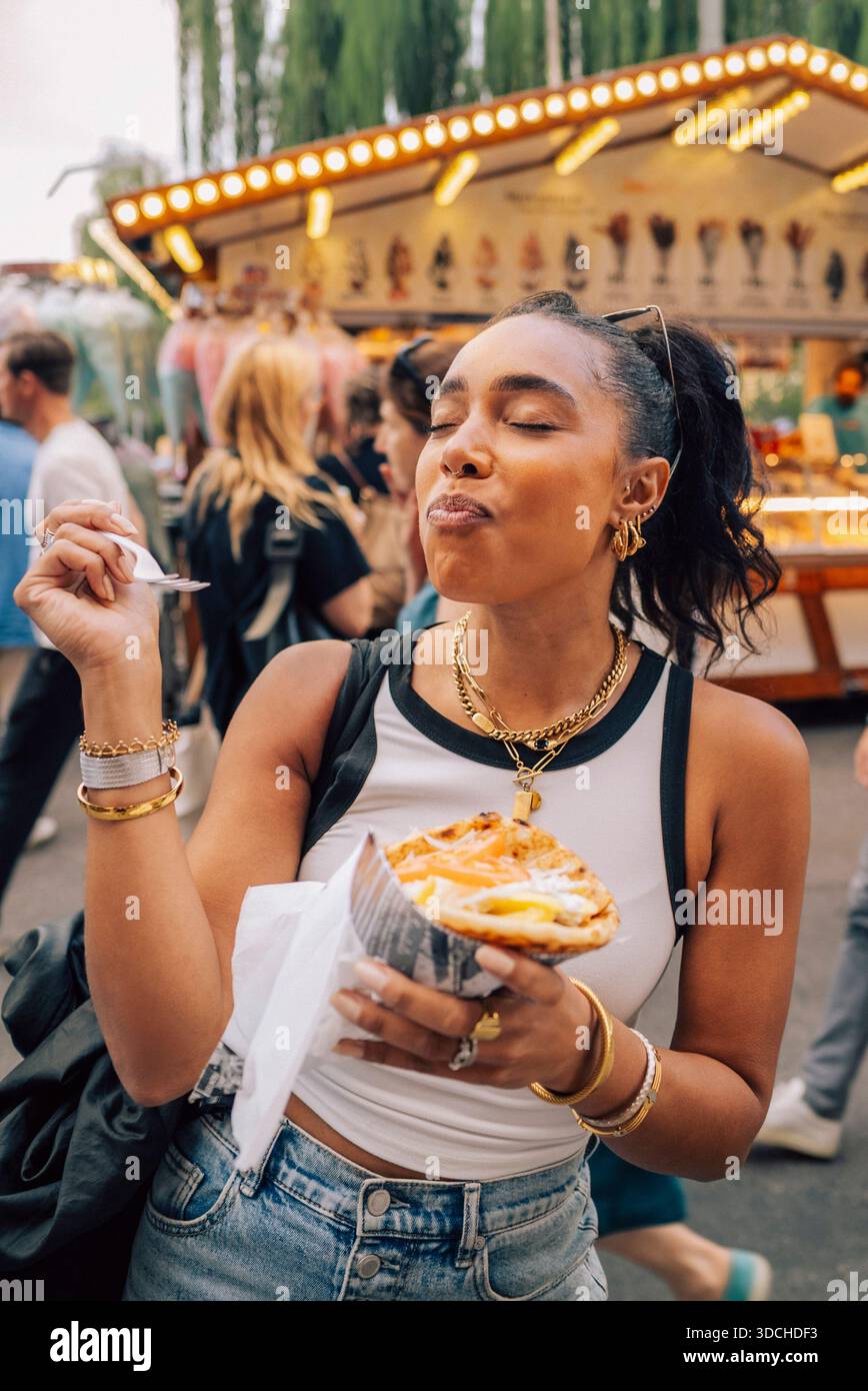 Femme insouciante mangeant des frites tout en profitant à la fête de rue Banque D'Images