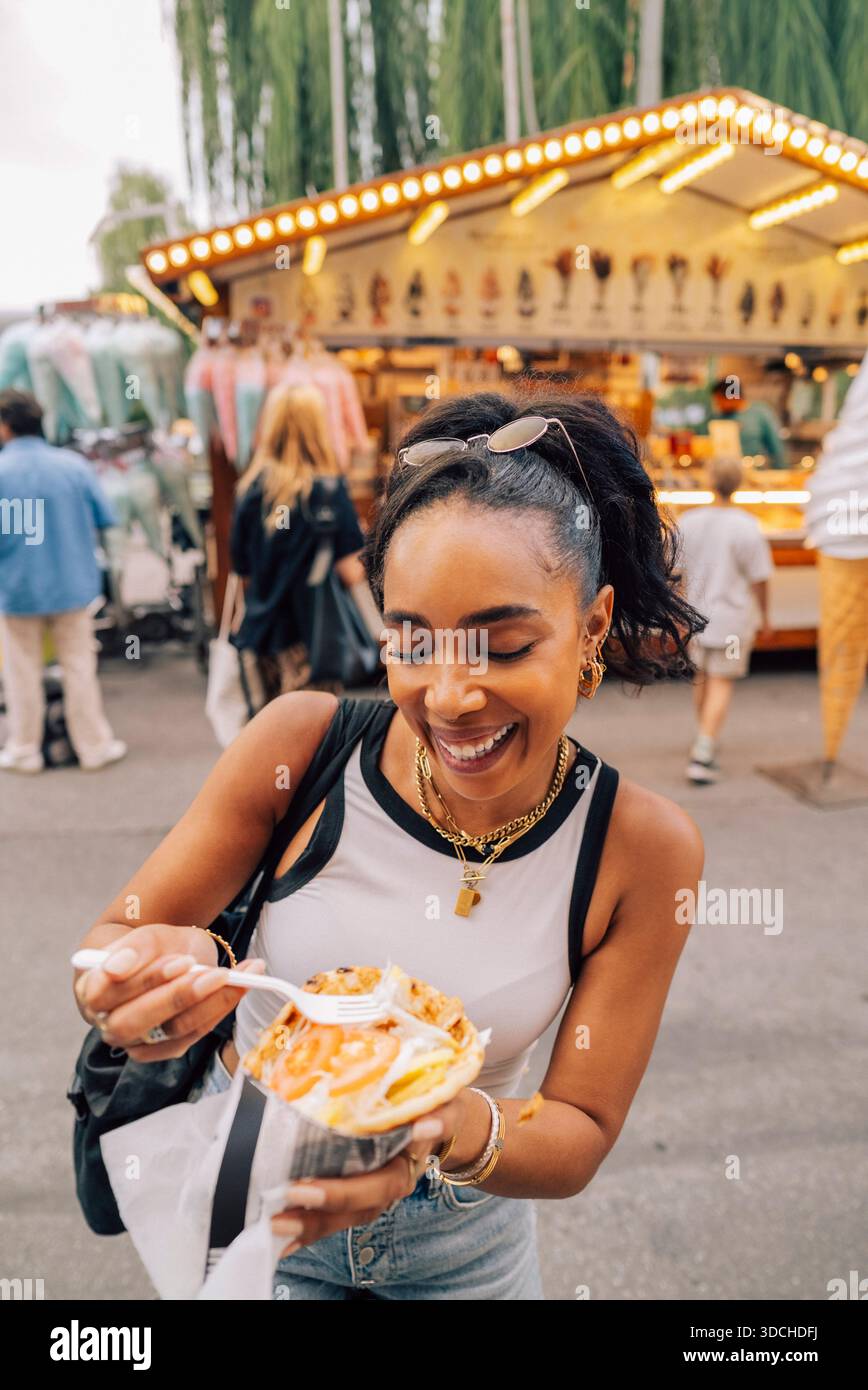 Vue en angle élevé de la femme heureuse mangeant des frites tout en profitant à la fête de rue Banque D'Images