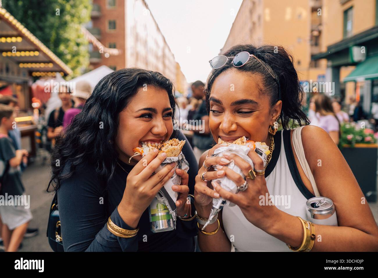 Amies féminines multiraciales mangeant sandwich enveloppé tout en appréciant au festival de la nourriture Banque D'Images