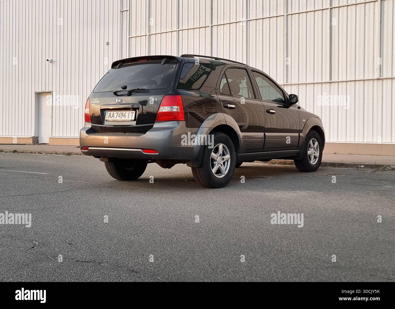 Noir KIA Sorento garé dans une rue. Vue arrière de trois quarts de SUV sombre dans le quartier industriel dans les faisceaux de soleil couchant. Banque D'Images