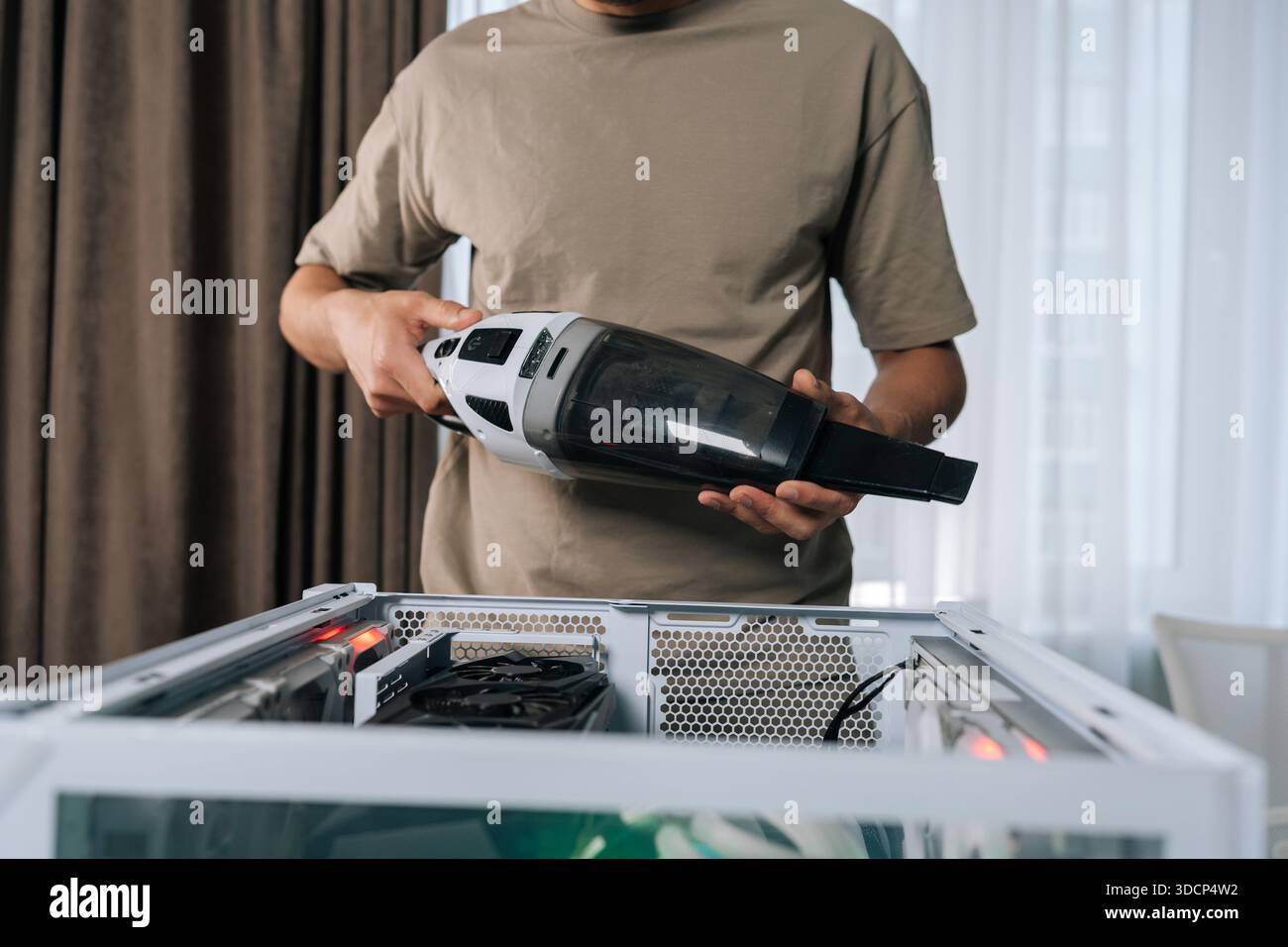 Photo recadrée d'un homme nettoyant les composants internes de l'ordinateur de bureau avec un aspirateur portable, garantissant des performances optimales et étendant le matériel Banque D'Images