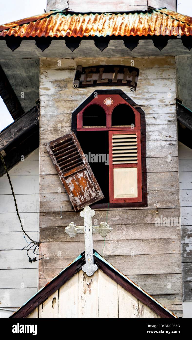 Une ancienne église en bois avec une fenêtre décorative, avec des volets ouverts et une croix sur la façade Banque D'Images