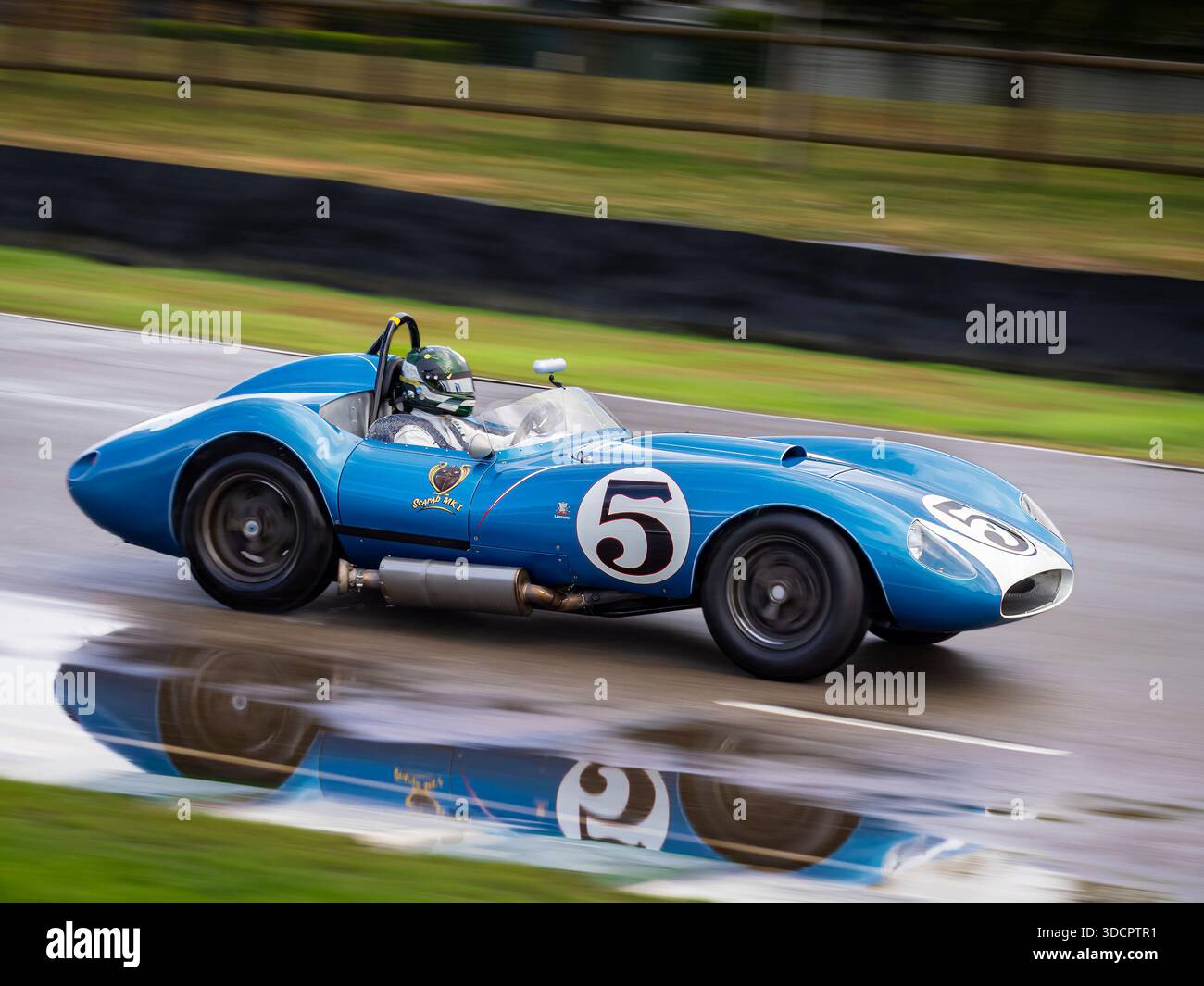 Une voiture de sport bleue Scarab Chevrolet Mk1 1958, roulant sous la pluie avec un reflet de la piste lors du Goodwood Revival 2025 Banque D'Images