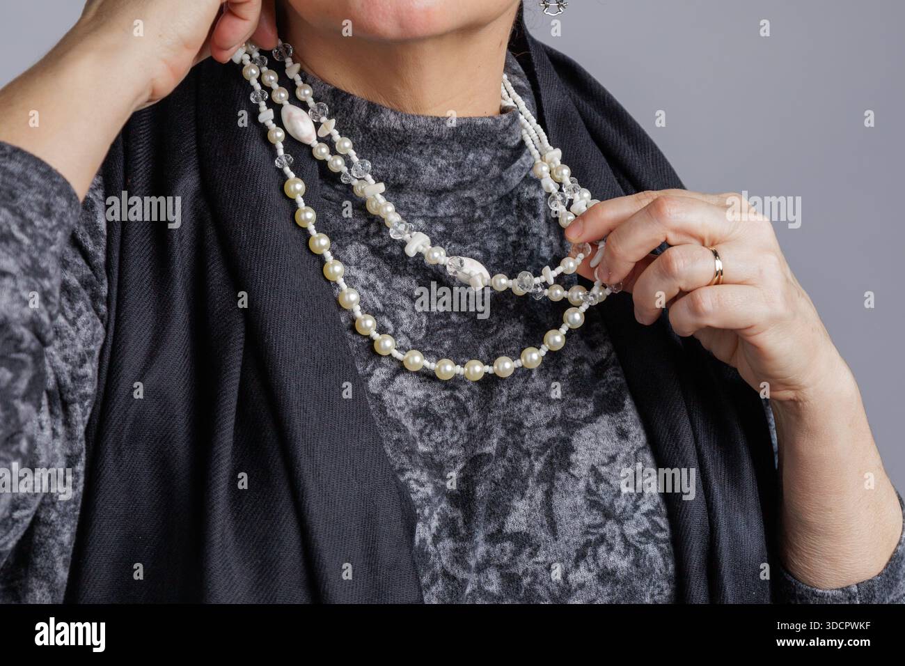 Gros plan des mains ajustant un collier de perles superposées contre une tenue texturée. Banque D'Images
