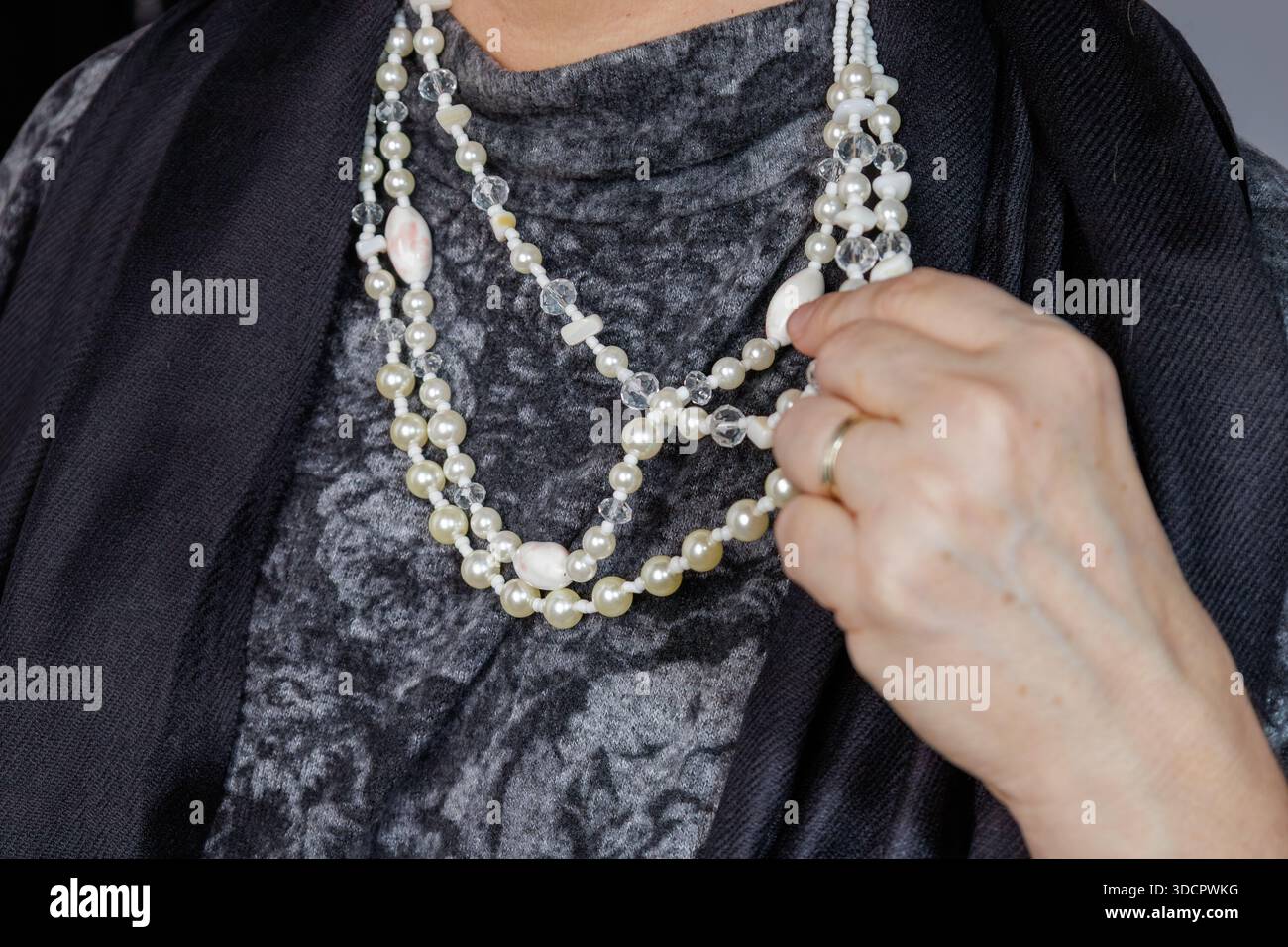 Gros plan d'un collier de perles superposées tenu par une main contre un tissu texturé. Banque D'Images