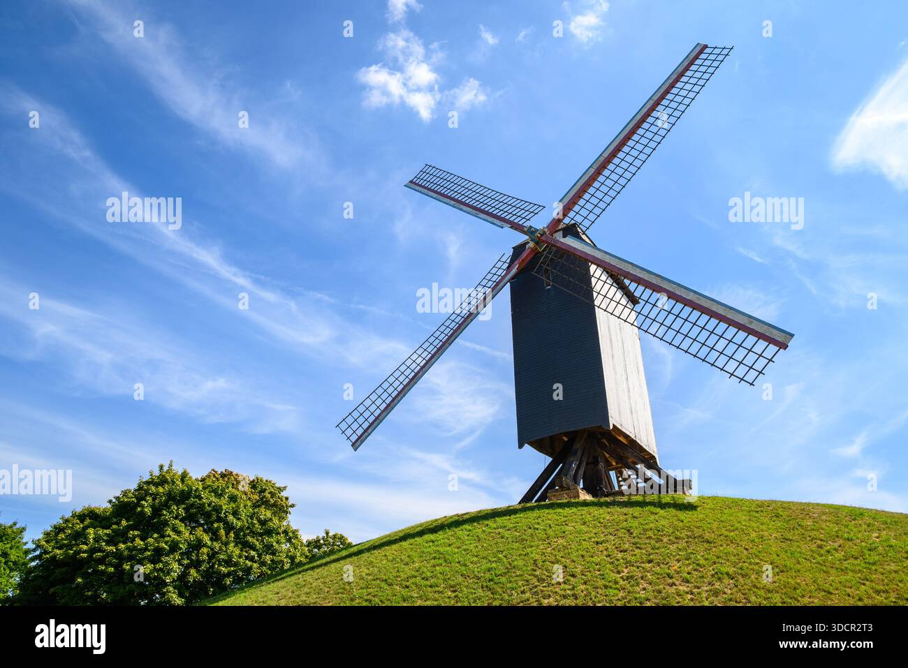 Moulin à vent traditionnel sur une colline herbeuse sous un ciel bleu. Banque D'Images