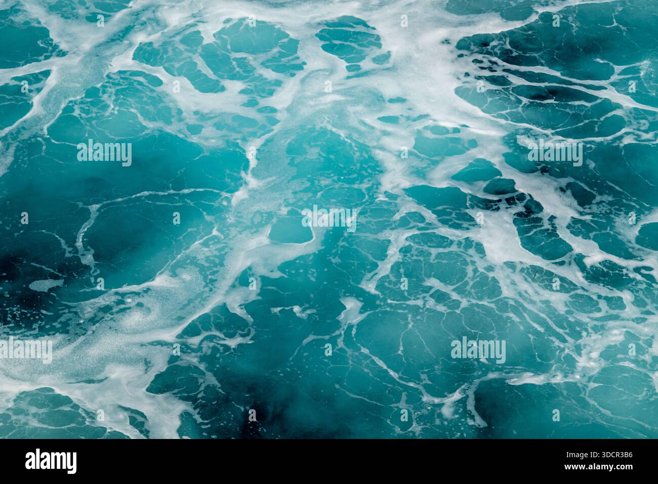 Vue aérienne des vagues turquoises de l'océan créant des motifs de mousse blanche. Banque D'Images
