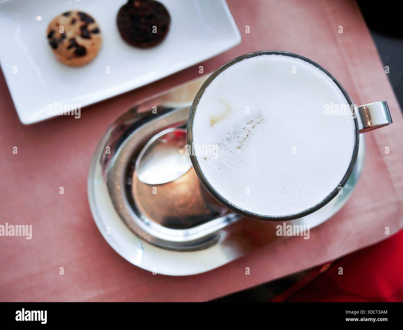 Photographie à plat représentant une tasse en verre de cappuccino chaud ou de latte recouverte d'une mousse de lait épaisse et crémeuse. Servi sur un plateau ovale argenté brillant avec une théière Banque D'Images
