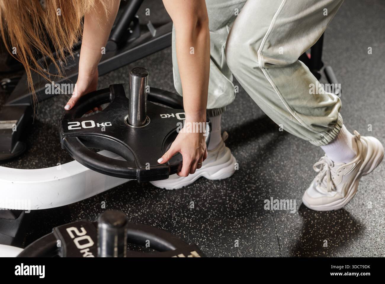 Gros plan des mains féminines chargeant la plaque de poids sur la barre se préparant à l'entraînement de force powerlifting dans le gymnase moderne Banque D'Images
