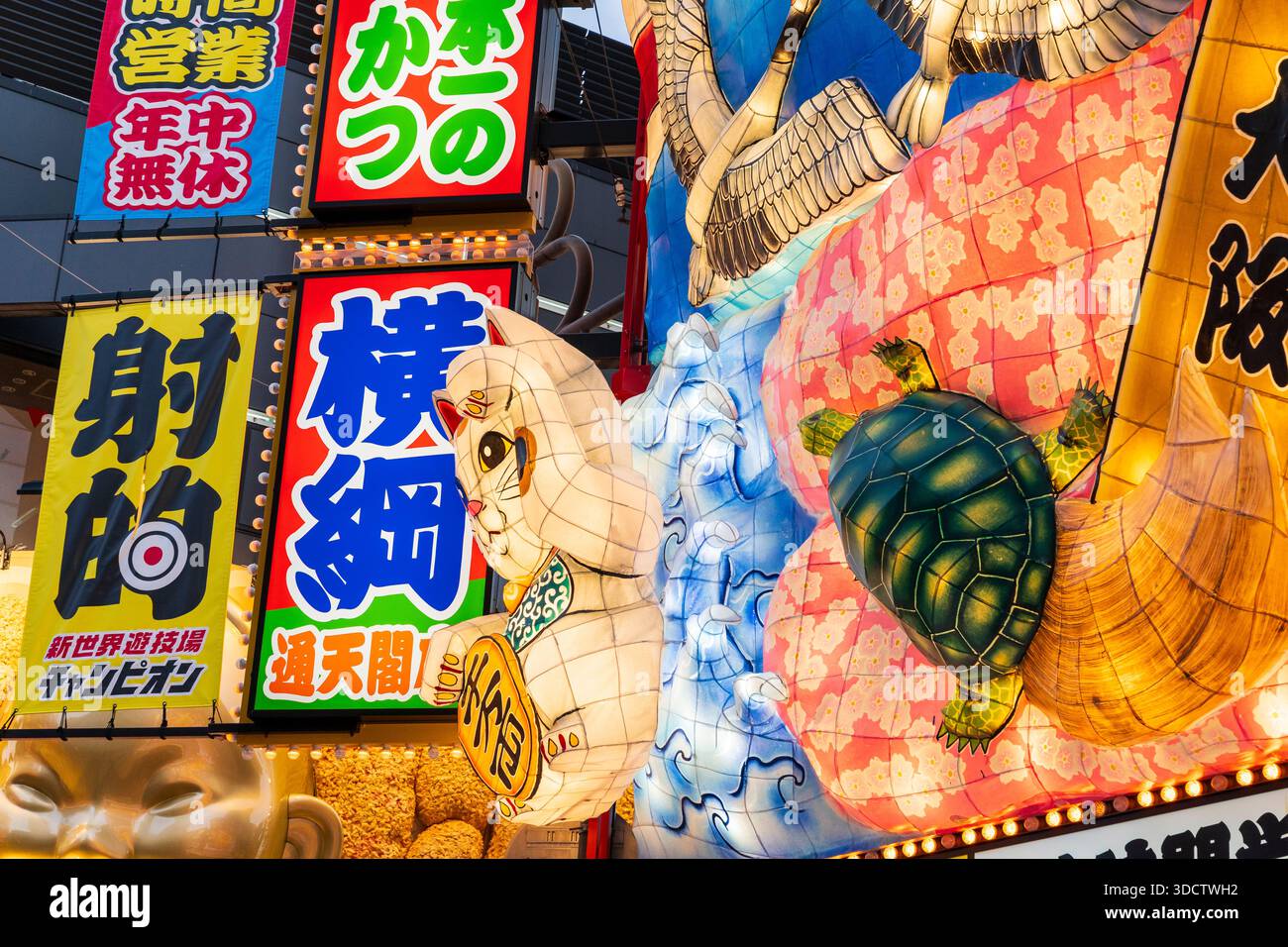 Chat chanceux japonais, Maneki-neko symbole de richesse, une grue et une tortue illuminée façade au-dessus de l'entrée d'un restaurant japonais à Shinsekai. Banque D'Images