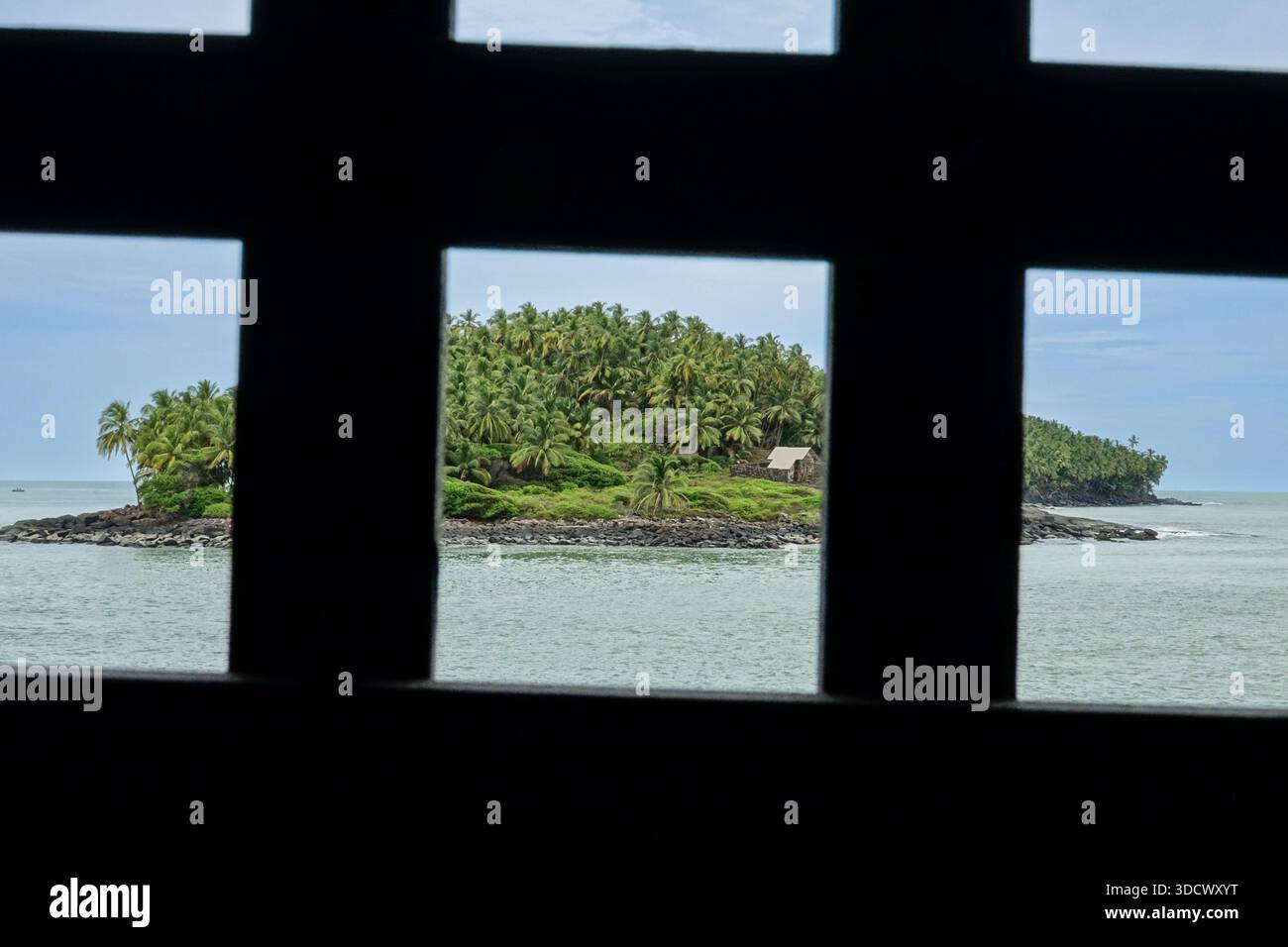 Une vue de la cabane en pierre entourée de cocotiers qui abritait le prisonnier politique français, le capitaine Alfred Dreyfus, sur l’île du Diable, vue depuis une cellule de prison sur l’île Saint-Joseph dans les colonies pénitentiaires des îles du Salut près de Kourou, en Guyane française. Dreyfus, un prisonnier politique a été maintenu en isolement au chalet de 1895 à 1899. Banque D'Images