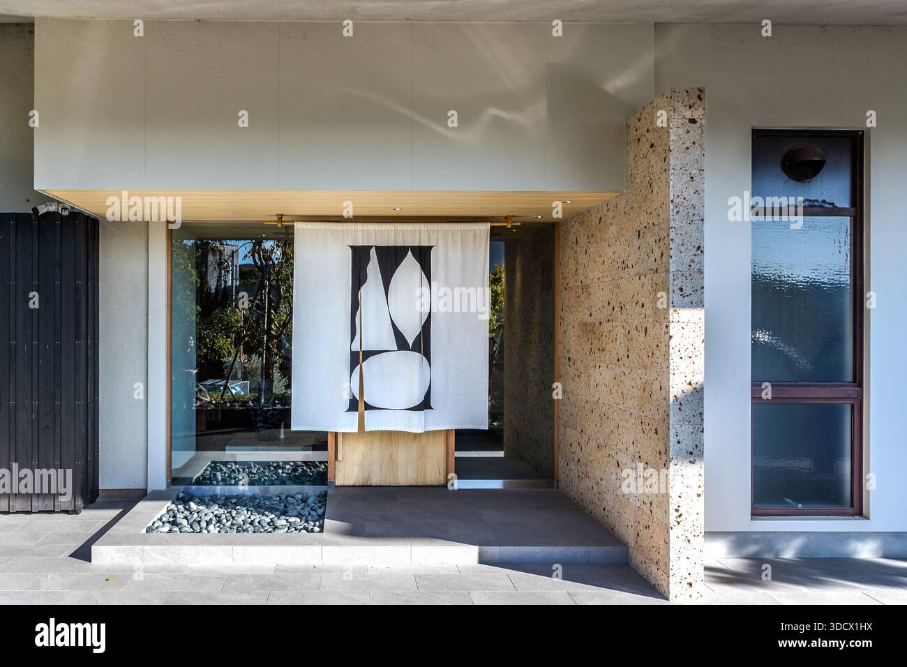 Un rideau noren avec un motif géométrique noir et blanc est suspendu devant l'entrée en bois du hôtel Kuroshio Sou à Shirahama. Des lits de gravier bordés de pierre bordent le chemin menant à l'entrée. Préfecture de Wakayama, Japon. Banque D'Images