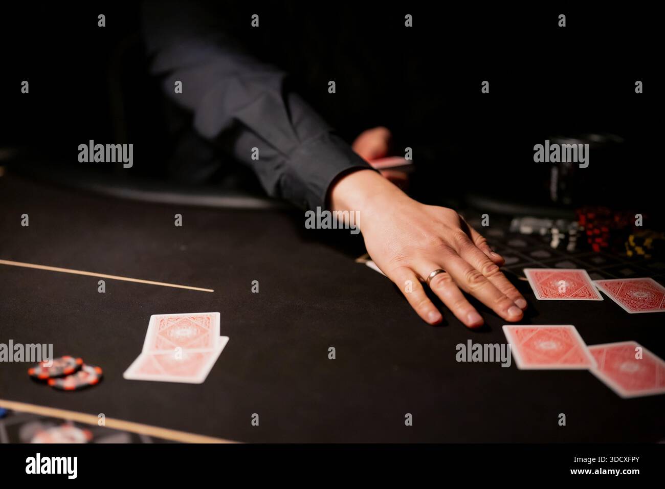 Détail de la table de poker de casino montrant la main du croupier arrangeant les cartes à jouer près des jetons et la disposition de pari, action de jeu ciblée dans l'intérieur sombre Banque D'Images