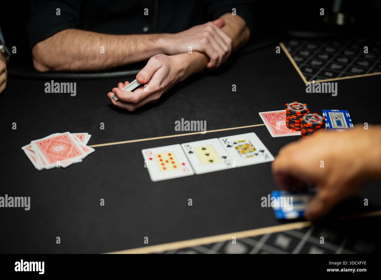 Scène de table de poker de casino en direct montrant les mains du croupier et des joueurs, les cartes communautaires révélées et les jetons empilés pendant les opérations de jeu réglementées Banque D'Images