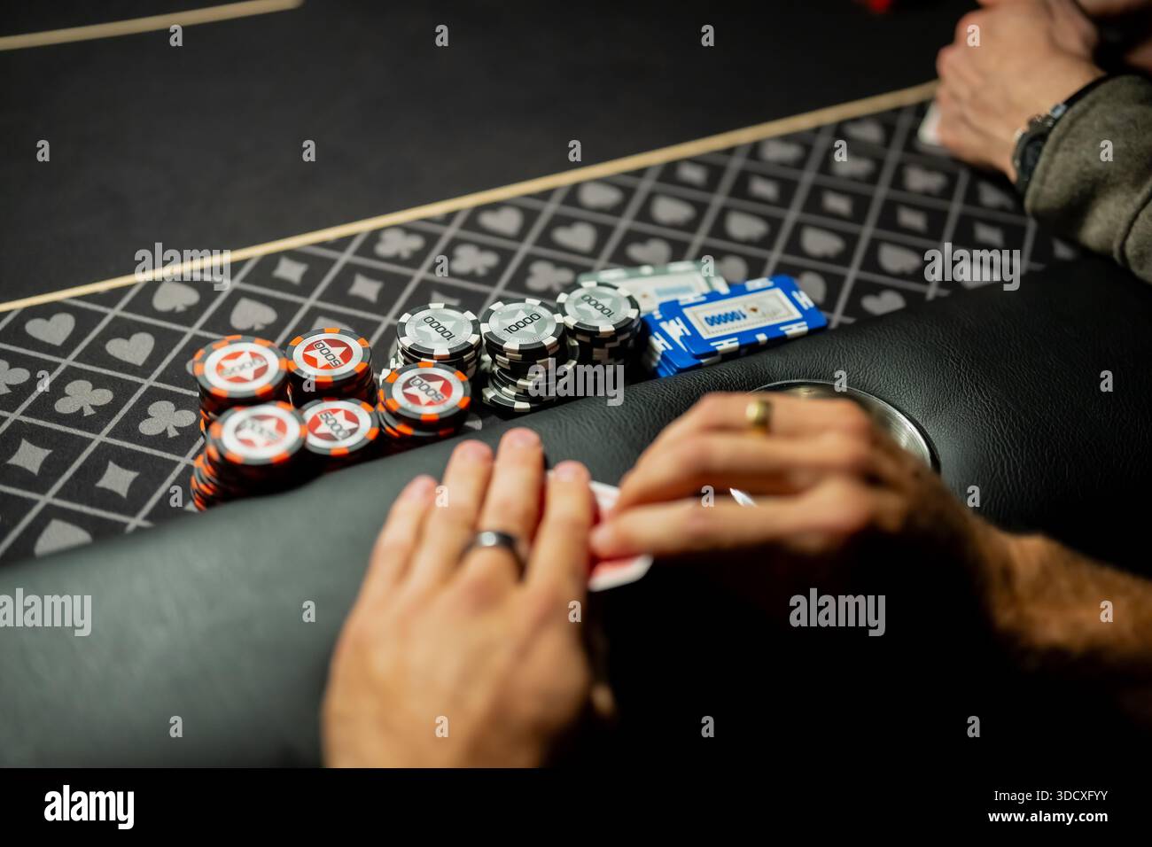 Détail de la table de poker du casino montrant les mains des joueurs protégeant les cartes à côté des jetons de Paris empilés, mettant en évidence le comportement de mise et la gestion des risques dans Li Banque D'Images