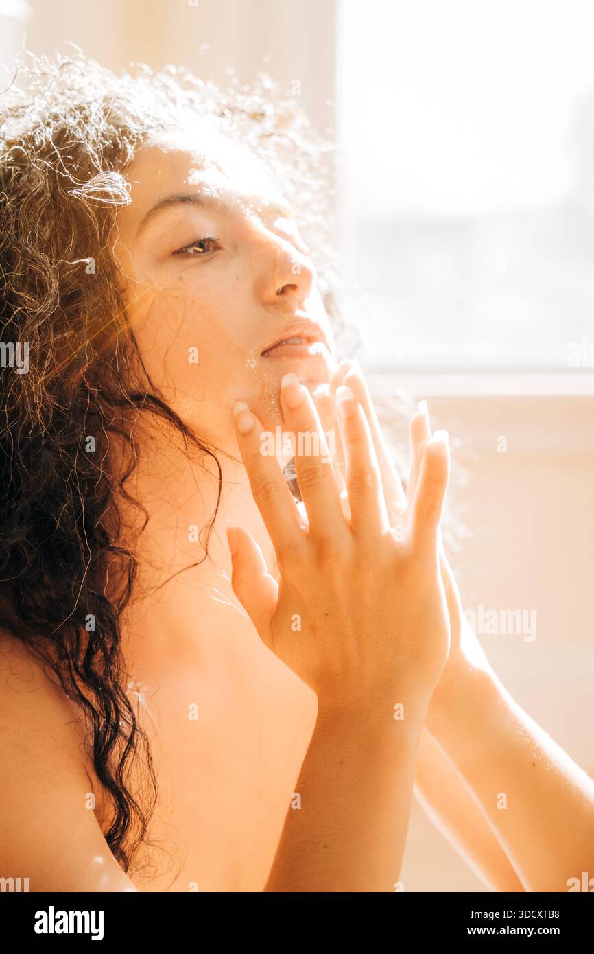 Femme appliquant le nettoyant visage pendant la routine de beauté du matin Banque D'Images