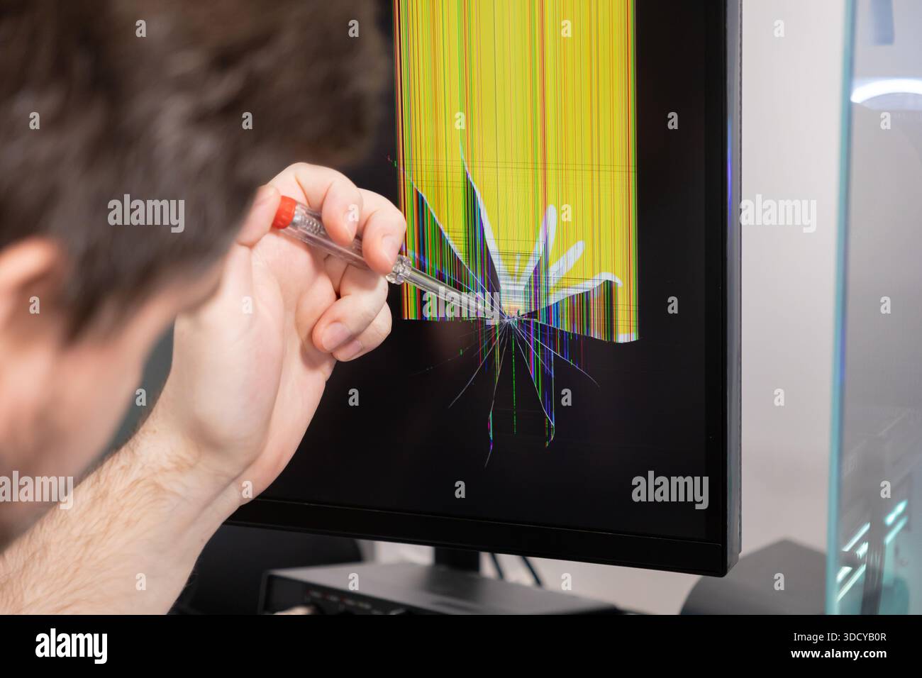 La main vise le tournevis à l'écran cassé du moniteur, montrant des lignes verticales vibrantes et une fissure en forme d'étoile, transportant la défaillance du matériel électronique et urgente Banque D'Images