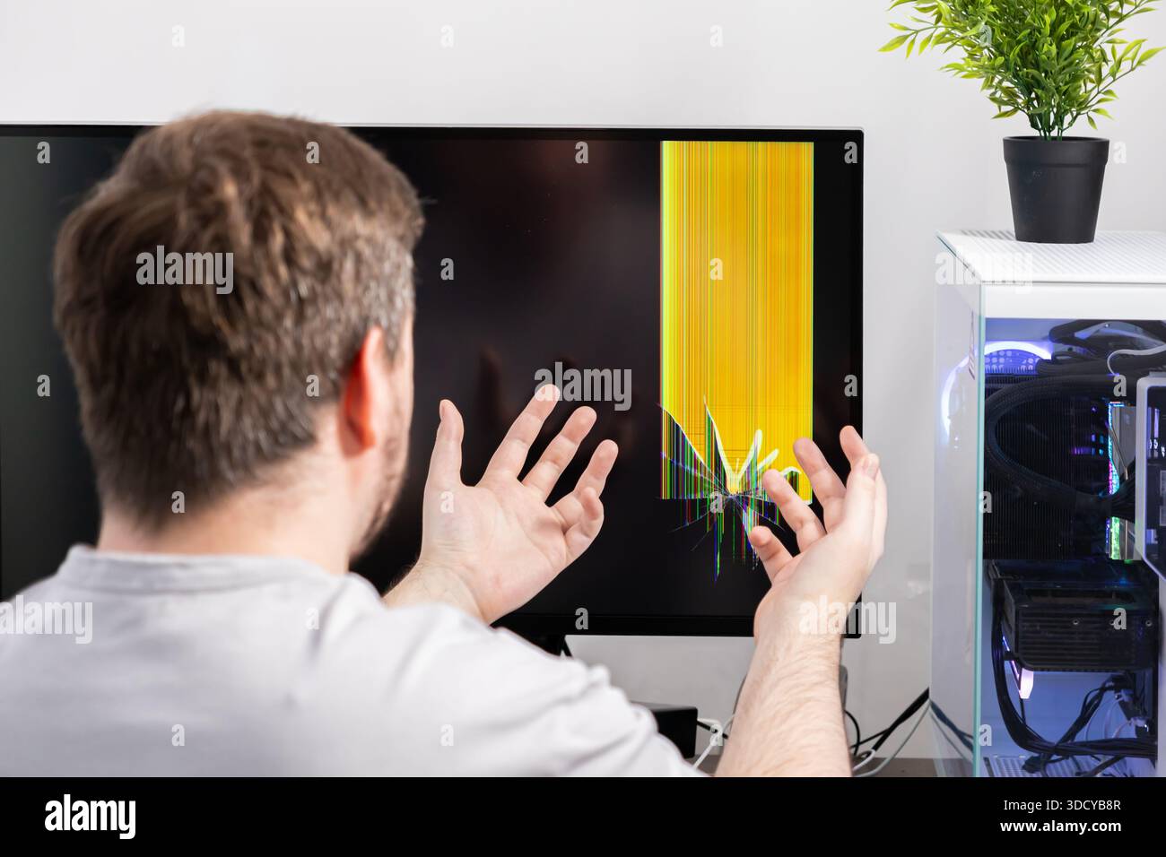 Gros plan d'une personne réagissant avec consternation à un écran d'ordinateur de bureau montrant un écran gravement cassé, des lignes jaunes, et une fissure visible, indicati Banque D'Images