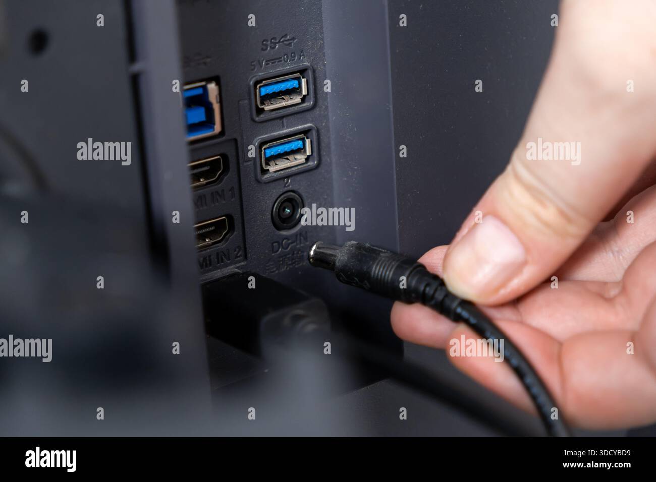 Gros plan d'une main connexion d'un cordon d'alimentation au port DC-IN situé à l'arrière d'un appareil, doté de ports USB et HDMI pour une connectivité électronique polyvalente Banque D'Images