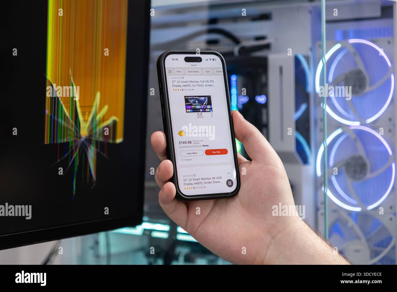 Poznan, Pologne - 2 novembre 2025 : la main utilise un smartphone pour parcourir de nouveaux moniteurs en ligne, soulignant le remplacement urgent d'un écran d'ordinateur fissuré fo Banque D'Images
