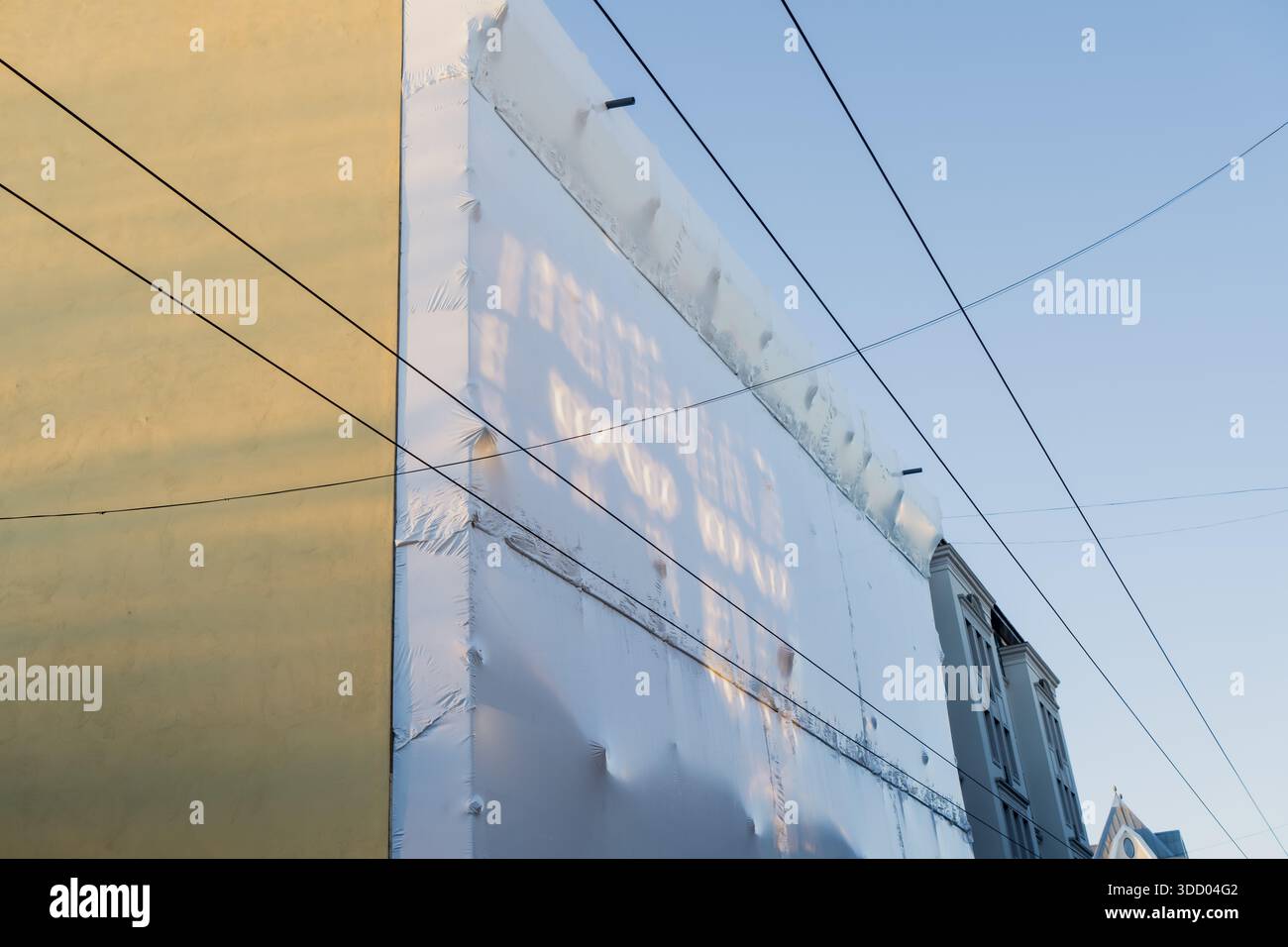 Mur de bâtiment rénové enveloppé d'une couche isolante et traversé par des fils électriques aériens, illustrant la construction urbaine, la restauration et les infrastes Banque D'Images