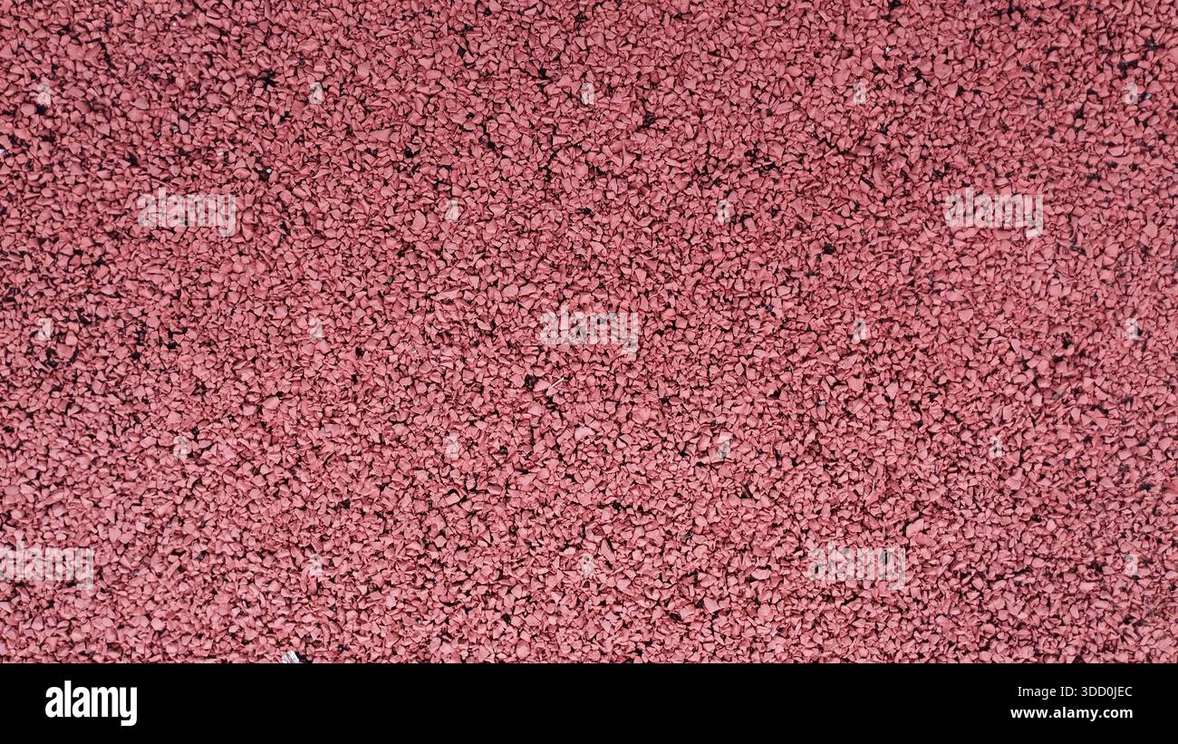 Une vue détaillée par le dessus montrant la texture granulaire d'une surface de piste de course en caoutchouc rouge. Banque D'Images