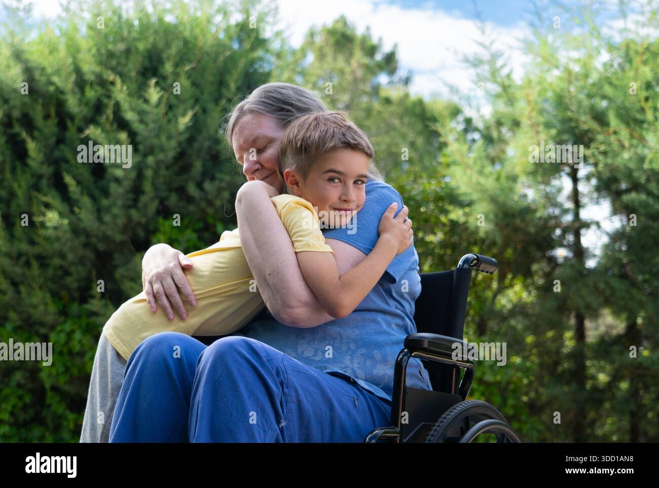 Grand-mère en fauteuil roulant embrassant petit-fils, exprimant l'amour et le lien familial au parc Banque D'Images