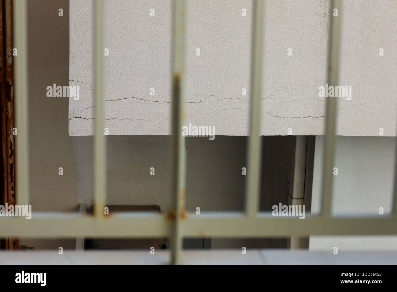Un mur fissuré vu à travers des barres métalliques rouillées, évoquant des thèmes de confinement, de négligence et des effets irréversibles du temps Banque D'Images