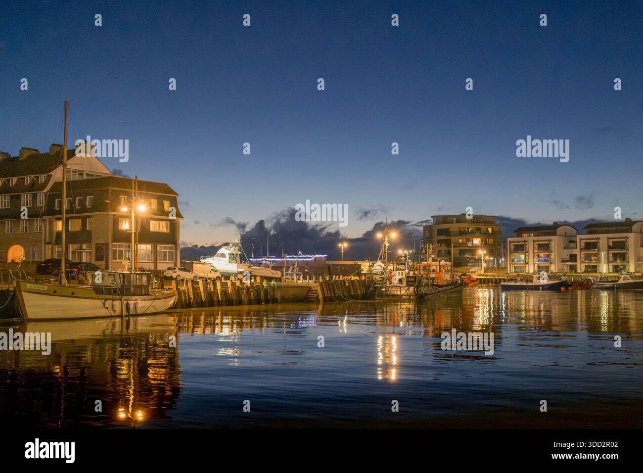 Port de Bridport au crépuscule avec un éclairage de rue subtil et discret qui vient juste sur et se reflète dans le port d'eau de mer. Banque D'Images
