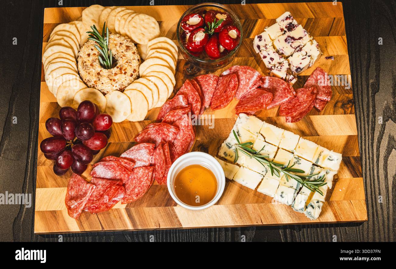 Belle planche de charcuterie avec salami, raisins, craquelins, assortiment de fromages, camembert cuit au four avec sauce aux fruits, fromage à la crème, poivrons farcis et miel Banque D'Images