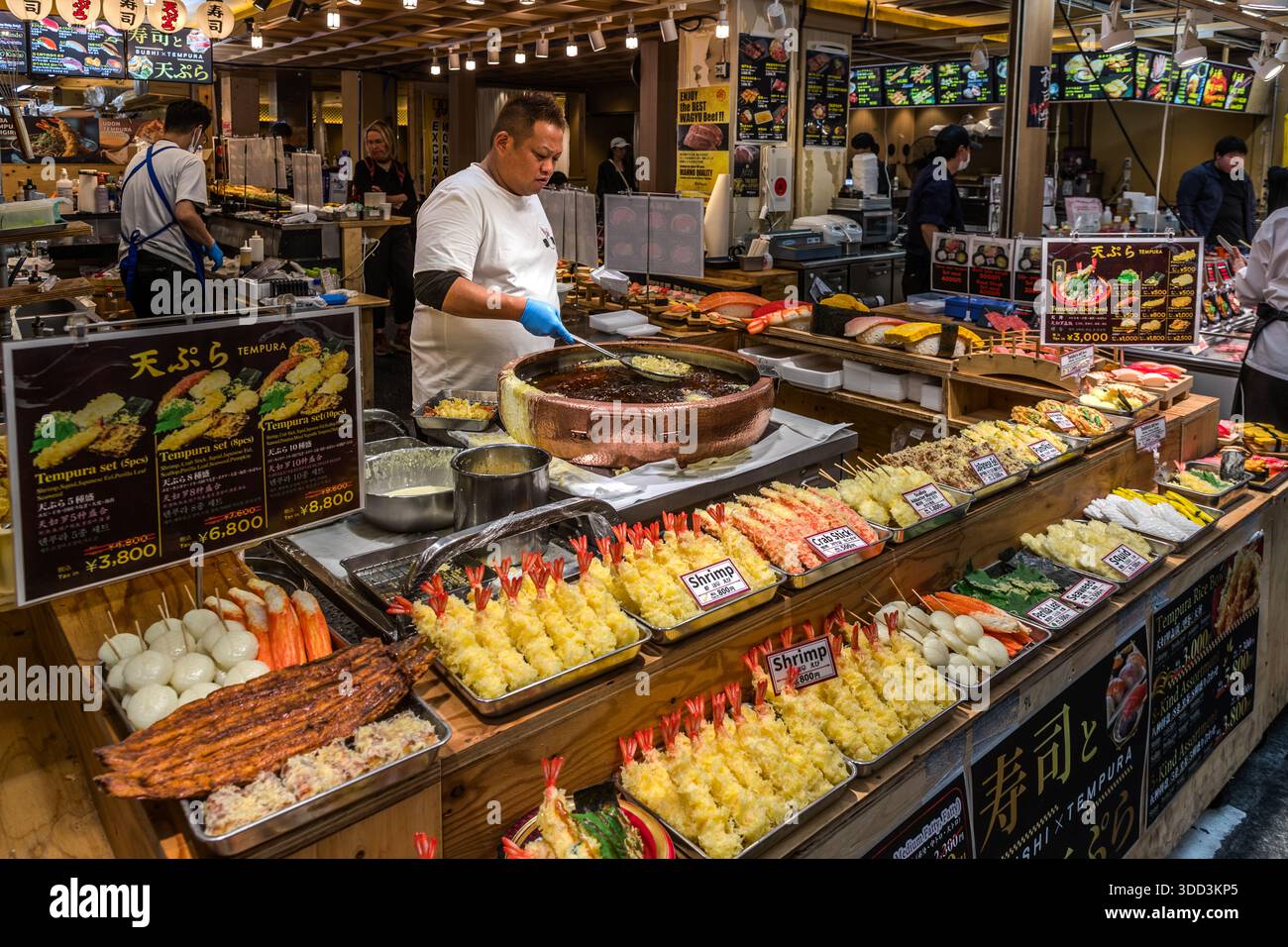 Un cuisinier fait frire des crevettes tempura et des bâtonnets de crabe dans une casserole en cuivre au marché Kuromon Ichiba à Osaka, au Japon. Banque D'Images