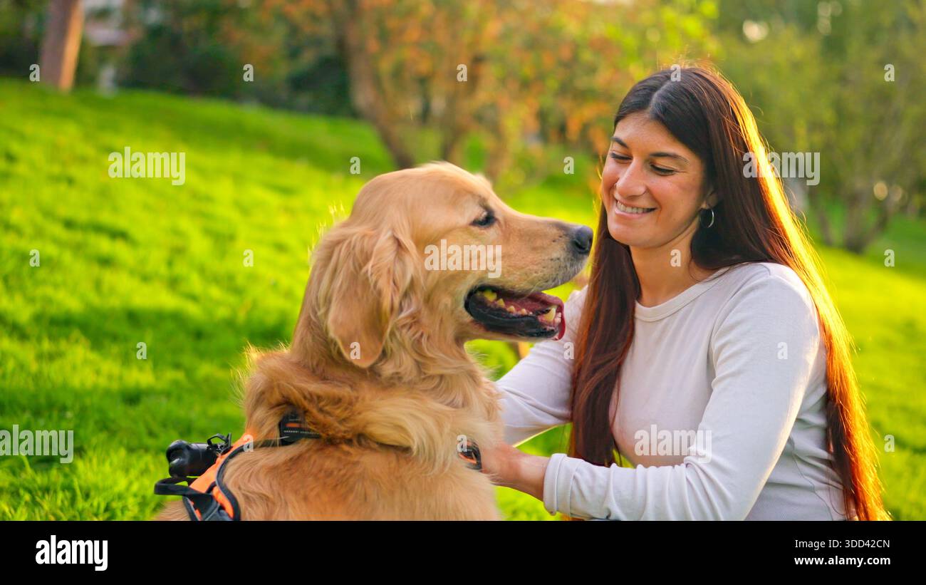 Femme souriant et caressant un chien Golden retriever dans le parc Banque D'Images