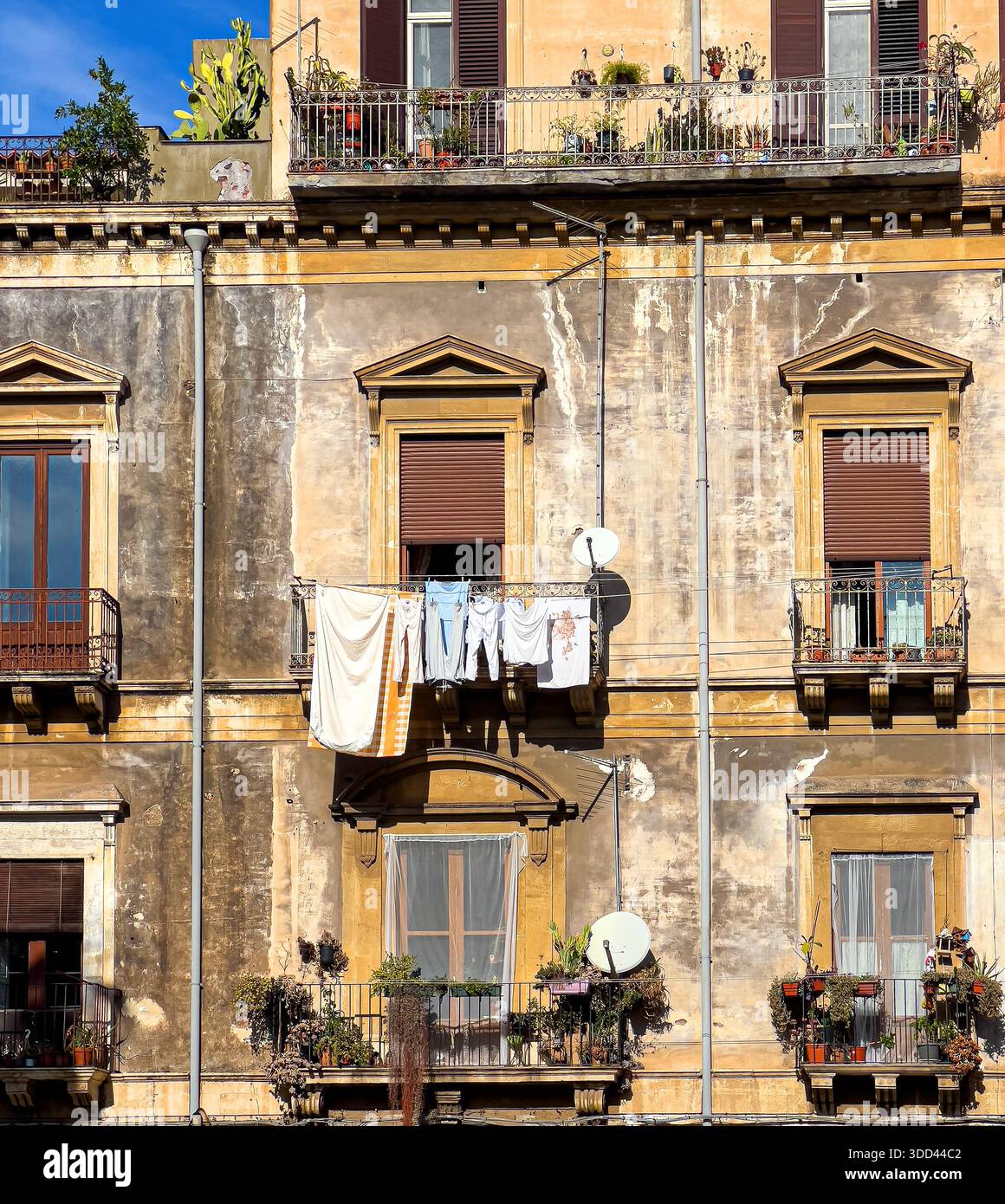 Ancien bâtiment avec peinture pelable, fenêtres, plantes et séchage des vêtements sur les balcons, Sicile. Italie Banque D'Images