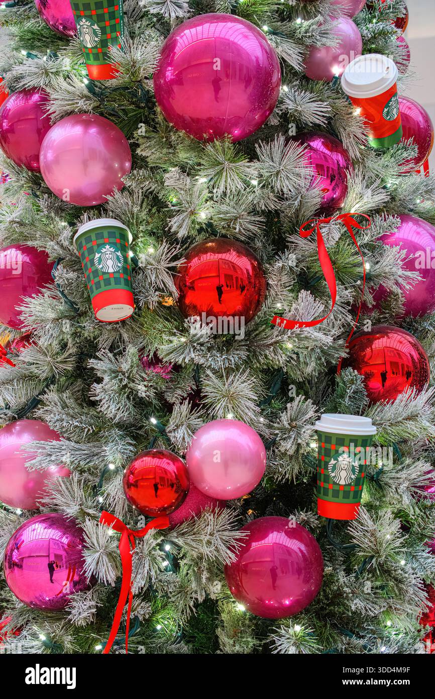 Gros plan d'un sapin de Noël décoré d'ornements roses et rouges, de lumières et de tasses Starbucks. Banque D'Images