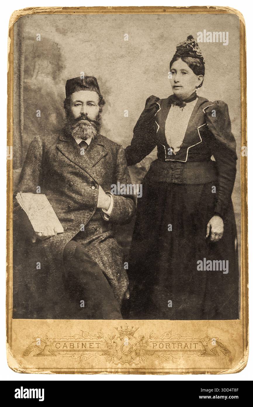 Portrait d'une famille juive de 1890 à 1910. Un homme barbu dans un costume et gilet formels, assis à côté d'une femme debout dans une robe. Un studio traditionnel Banque D'Images